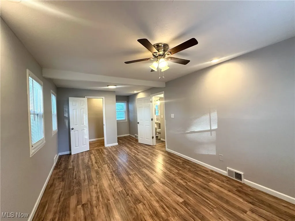 Unfurnished bedroom featuring dark wood-style floors, multiple windows, and ceiling fan