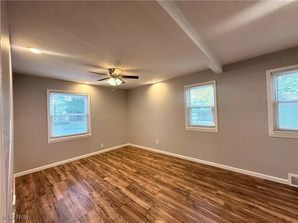 Unfurnished room with dark wood finished floors, beamed ceiling, and a ceiling fan
