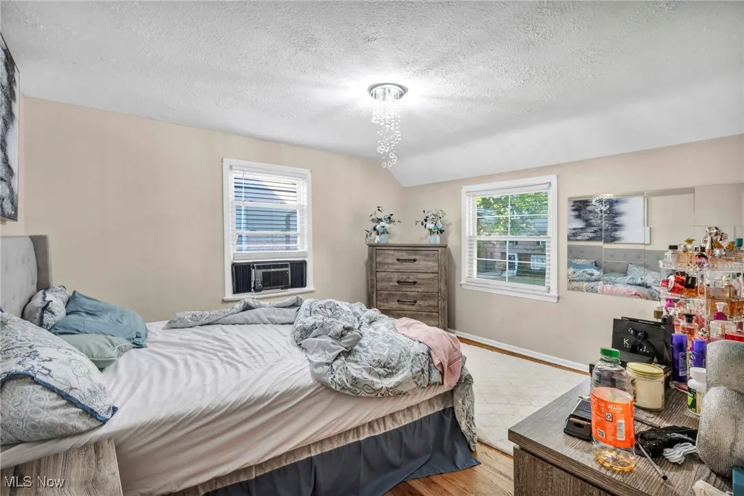 Bedroom with wood finished floors, a textured ceiling, and vaulted ceiling