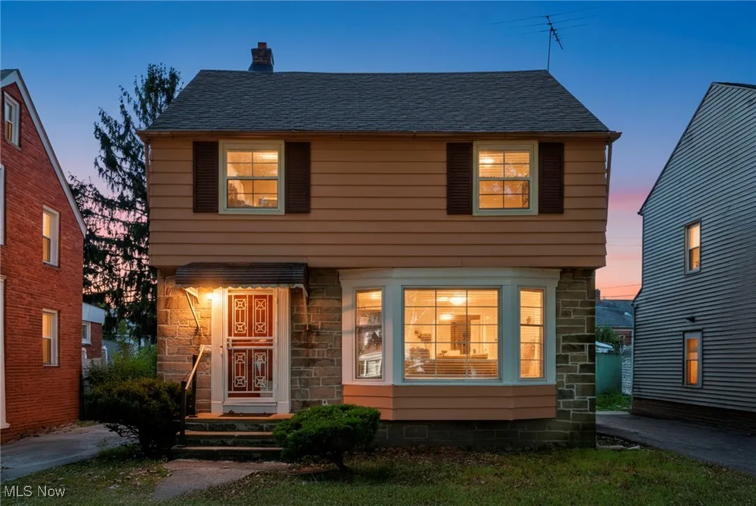 Colonial house featuring stone siding, a chimney, and a shingled roof