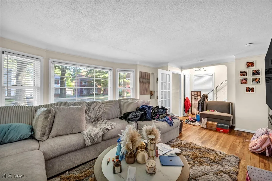 Living room with wood finished floors, a textured ceiling, ornamental molding, stairway, and arched walkways