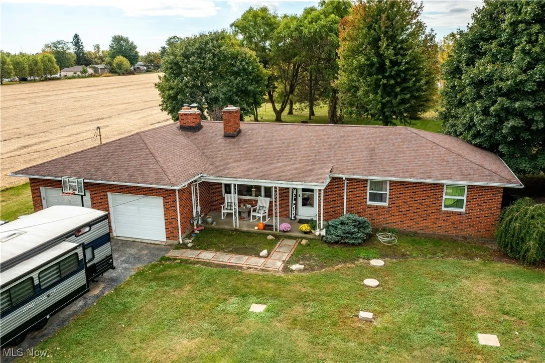 Ranch-style house featuring a chimney, brick siding, an attached garage, asphalt driveway, and a front yard