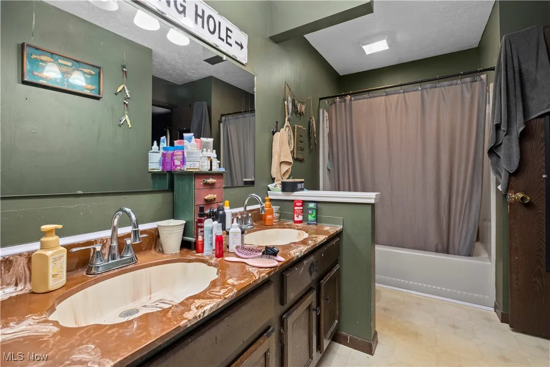 Bathroom with shower / bathtub combination with curtain, a textured ceiling, double vanity, and light floors
