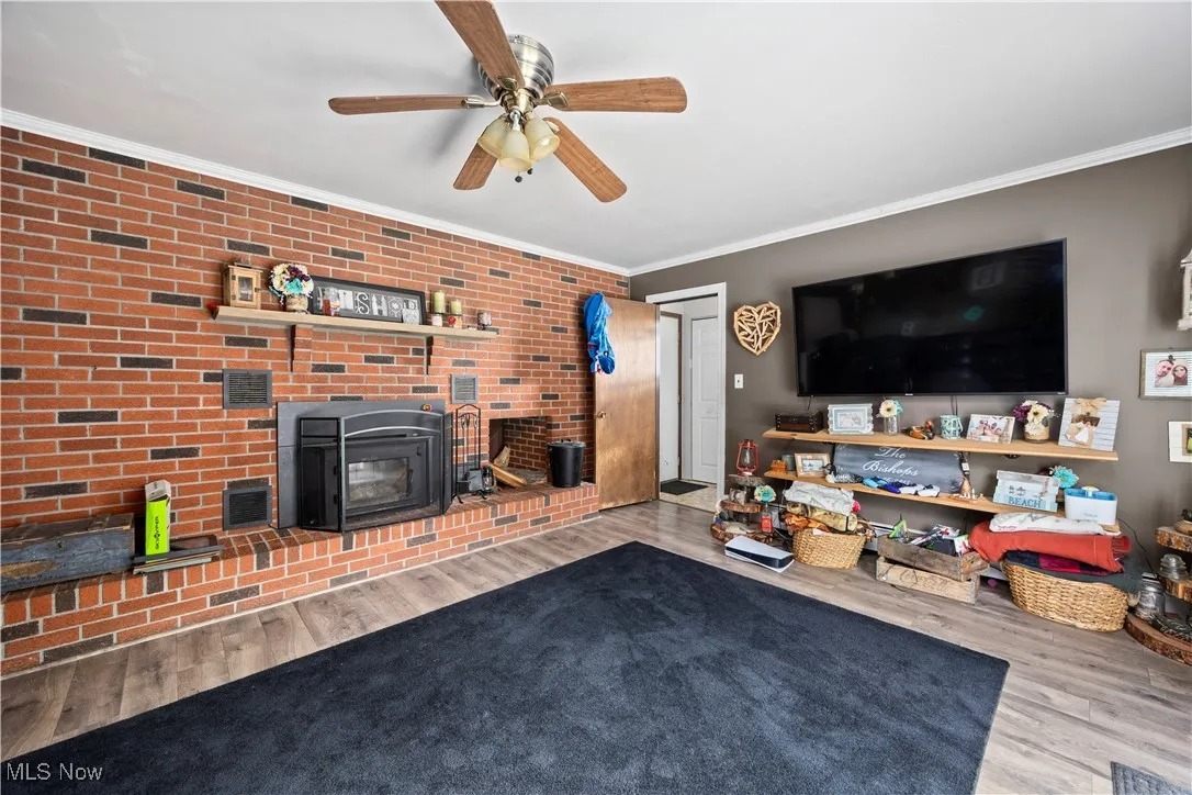 Living room featuring crown molding, wood finished floors, a ceiling fan, and brick wall