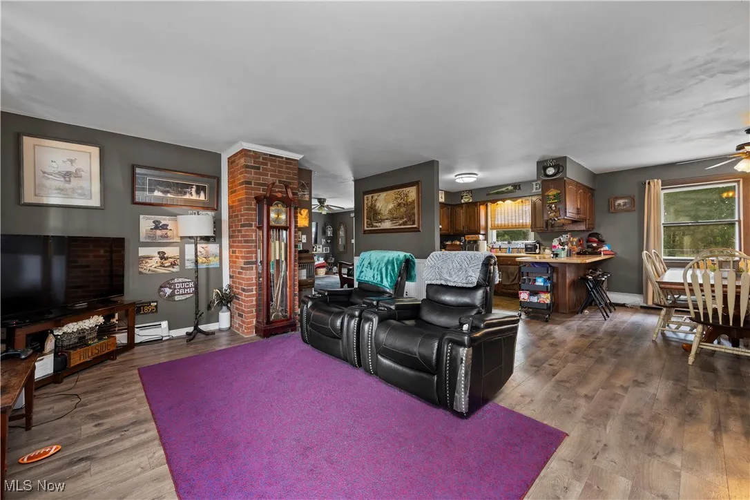 Living area featuring a ceiling fan, dark wood-style flooring, and a baseboard heating unit