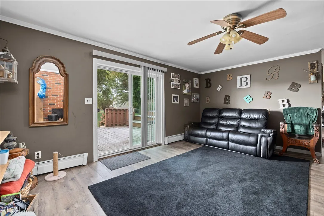 Living room featuring ornamental molding, light wood-type flooring, a baseboard heating unit, and ceiling fan