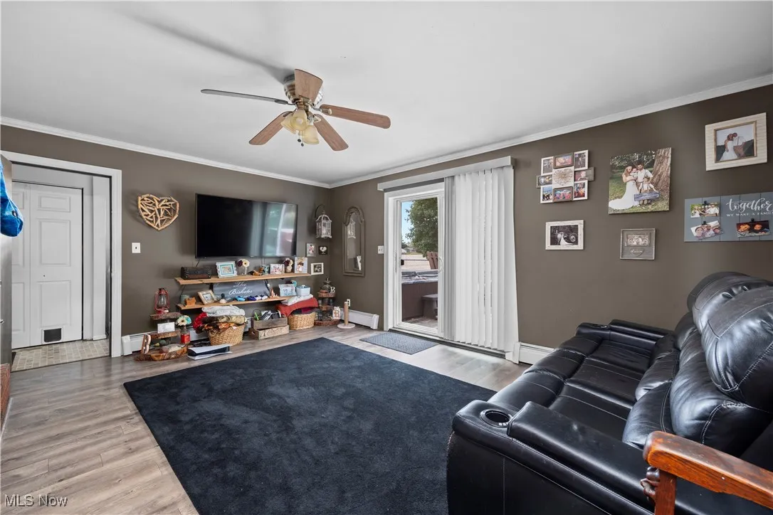 Living area with crown molding, wood finished floors, a ceiling fan, and a baseboard heating unit