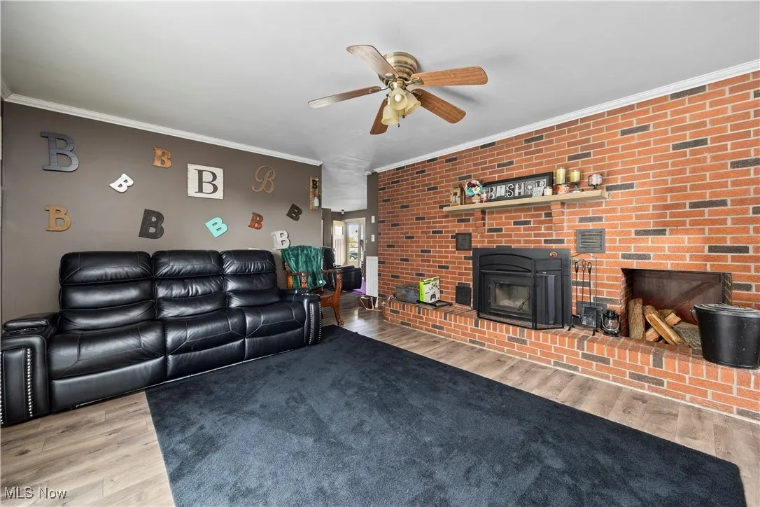 Living room featuring crown molding, a fireplace, brick wall, light wood-style floors, and ceiling fan
