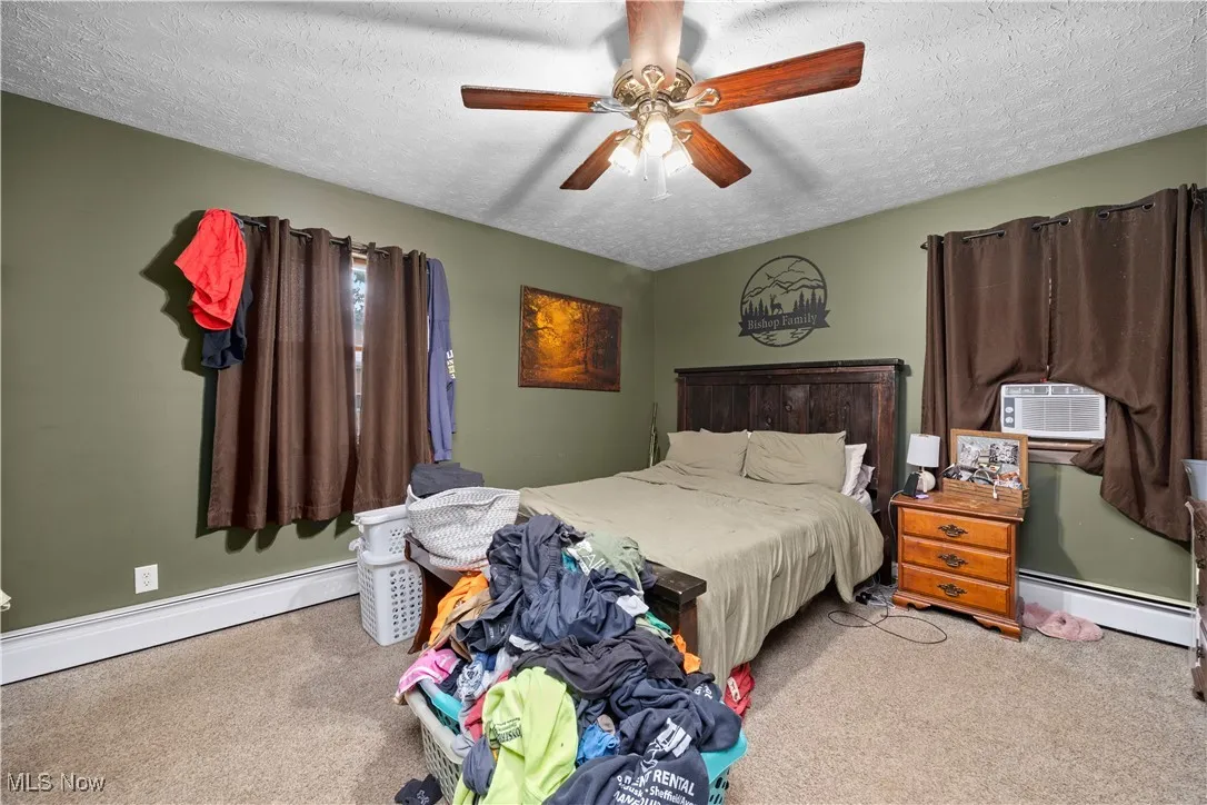 Carpeted bedroom with a textured ceiling, a baseboard radiator, ceiling fan, and cooling unit