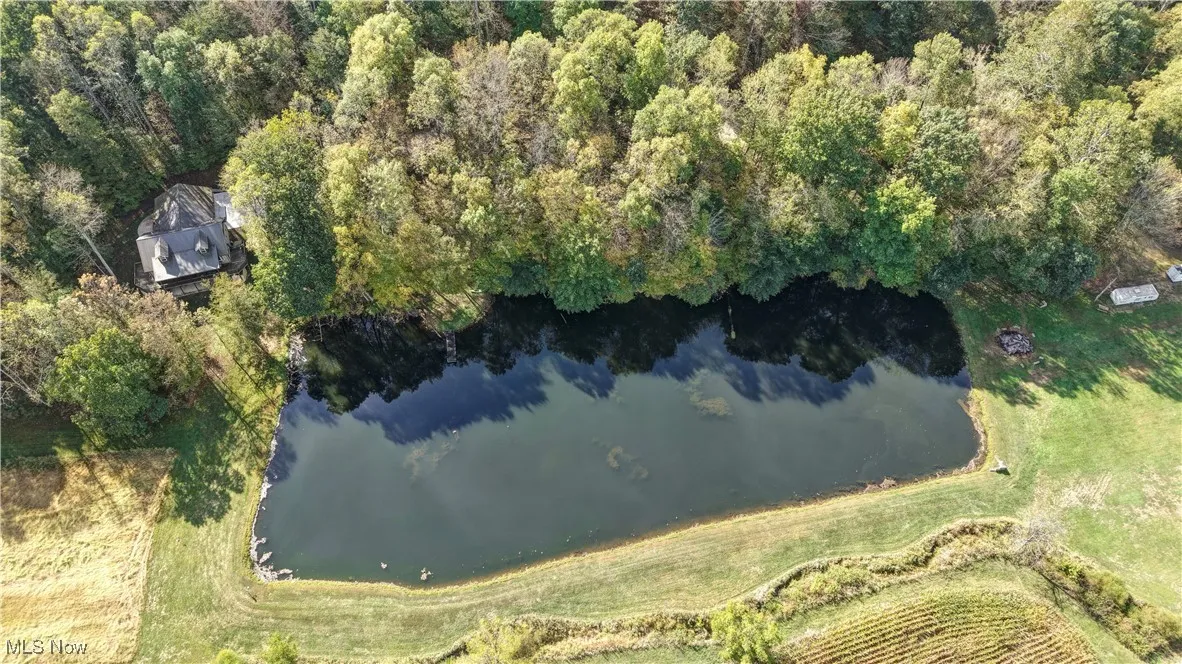 Aerial view of property and surrounding area featuring a nearby body of water and a heavily wooded area