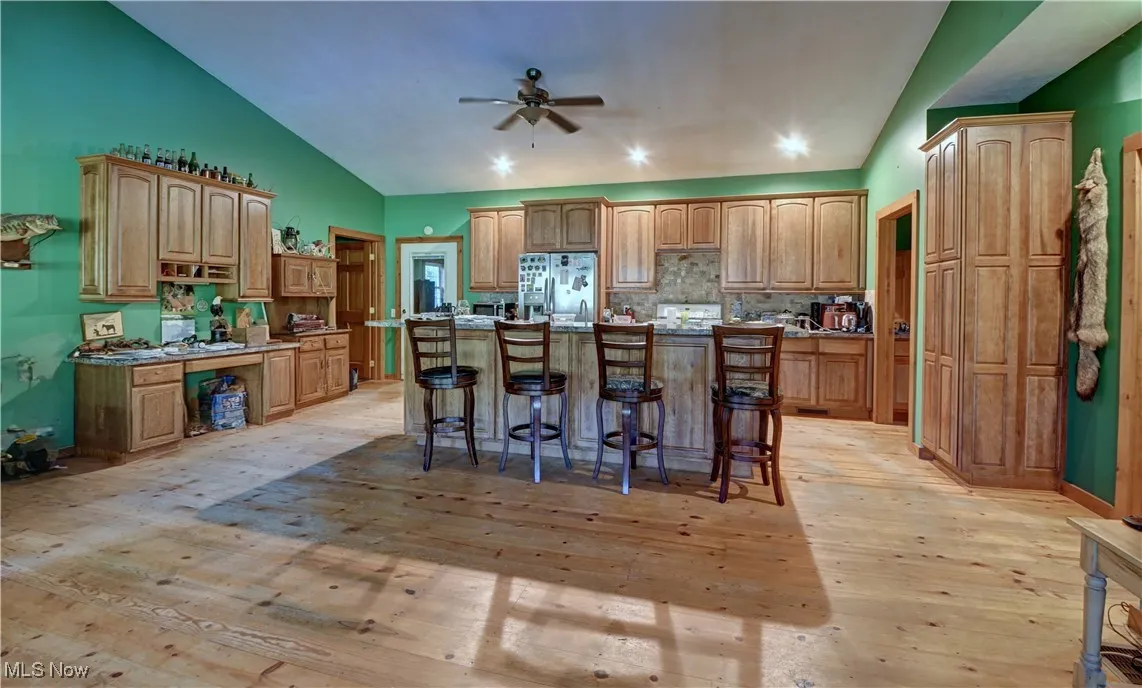 Kitchen featuring a kitchen breakfast bar, light wood-style flooring, decorative backsplash, a kitchen island with sink, and fridge with ice dispenser