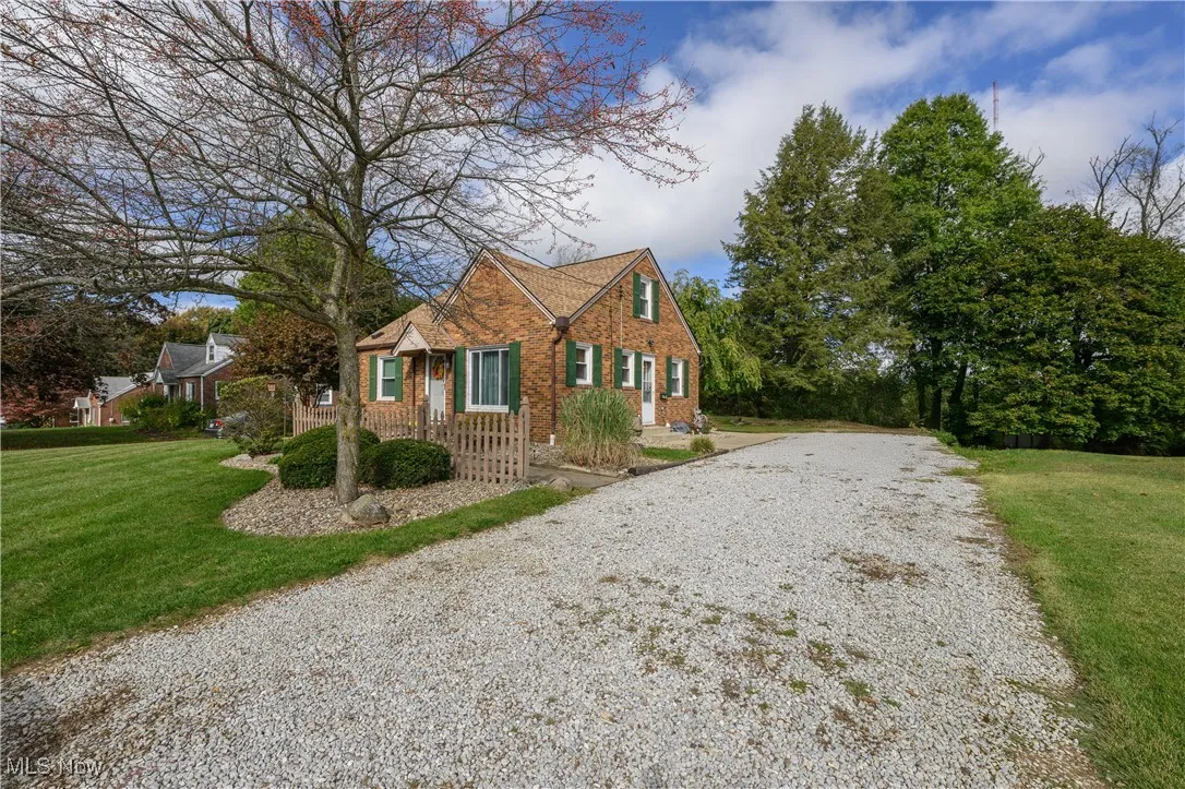 View of side of property featuring gravel driveway, a yard, and brick siding