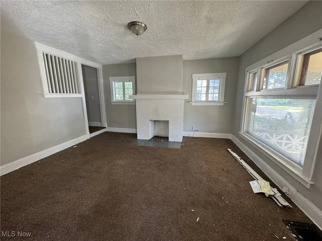 Unfurnished living room with dark carpet, a textured ceiling, and a brick fireplace