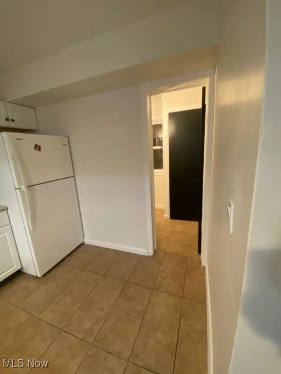 Kitchen featuring freestanding refrigerator, light tile patterned floors, and white cabinets