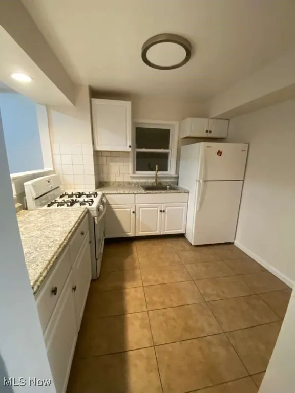 Kitchen with white cabinetry, light countertops, white appliances, decorative backsplash, and light tile patterned floors