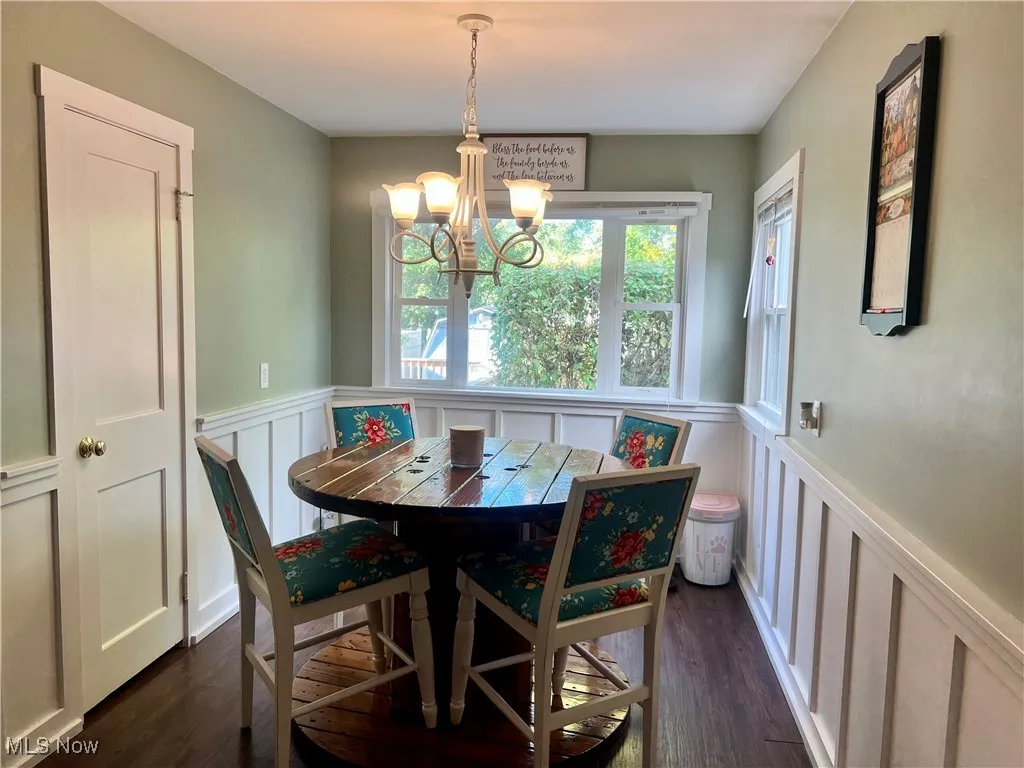 Dining room with a chandelier, a wainscoted wall, a decorative wall, and dark wood-style floors