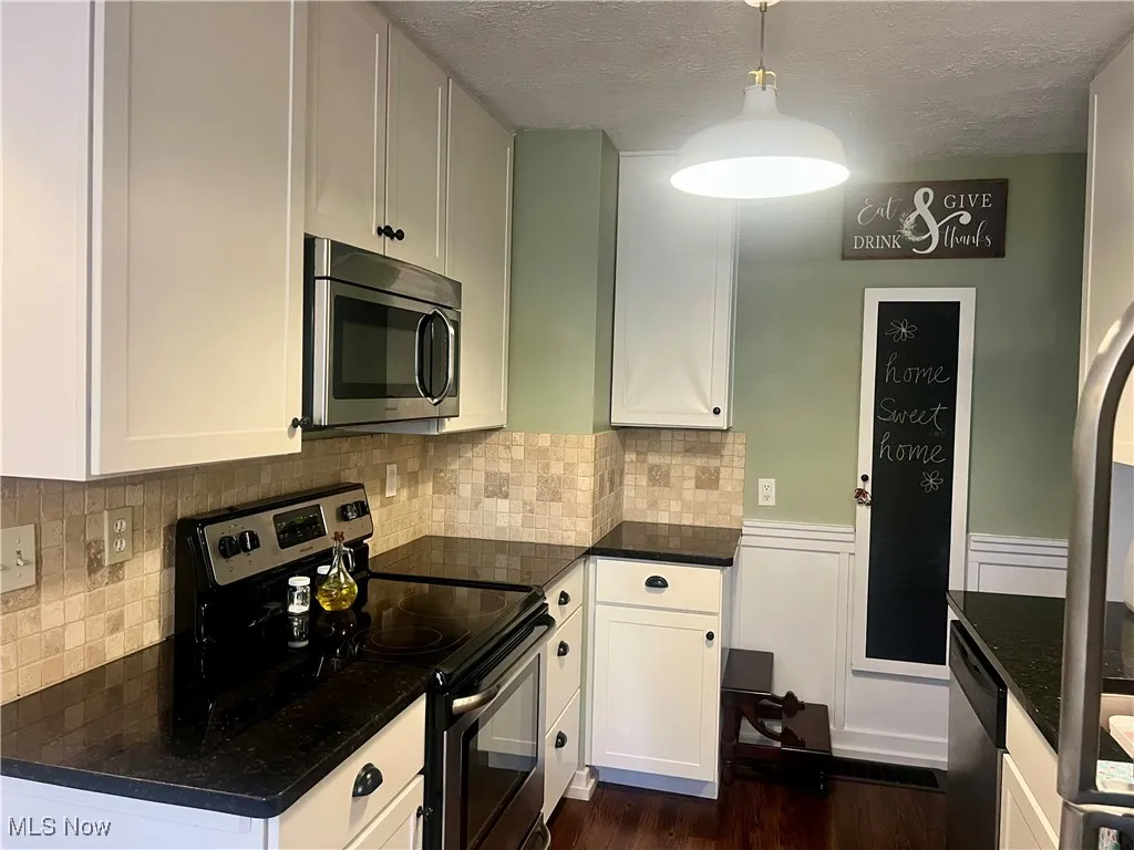 Kitchen featuring stainless steel appliances, decorative backsplash, pendant lighting, dark wood-style flooring, and dark stone counters