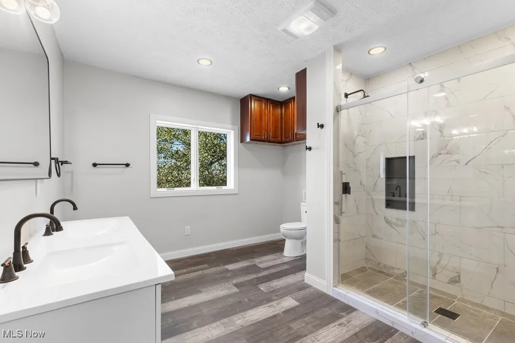 Bathroom with a textured ceiling, double vanity, dark wood-type flooring, a marble finish shower, and recessed lighting