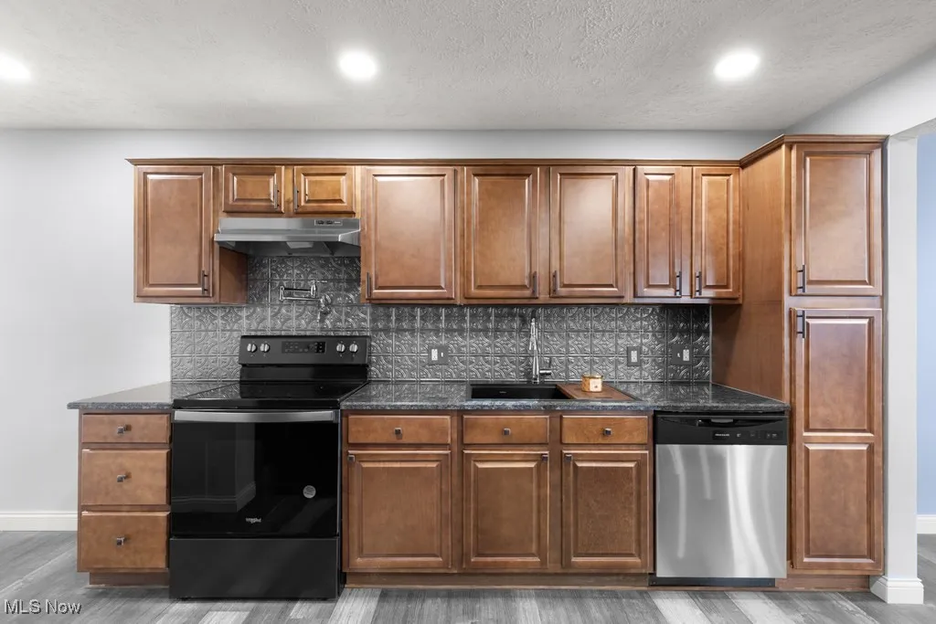Kitchen with range with electric cooktop, stainless steel dishwasher, dark stone counters, decorative backsplash, and recessed lighting