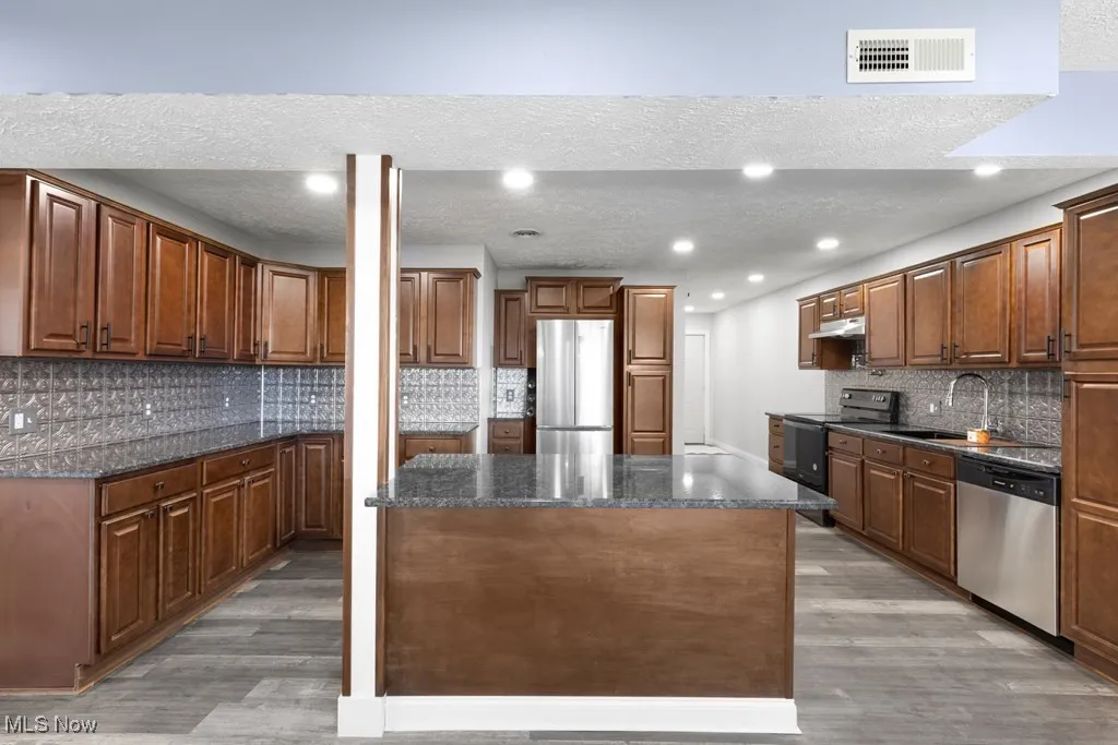 Kitchen featuring decorative backsplash, a textured ceiling, light wood finished floors, appliances with stainless steel finishes, and a kitchen island