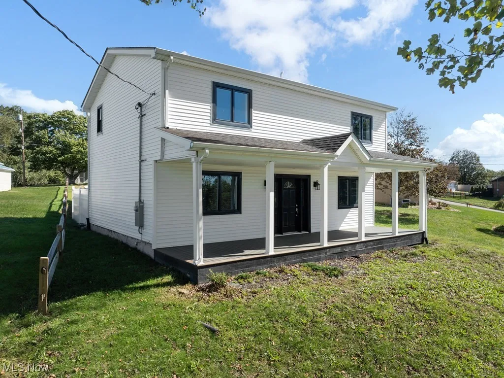 Back of property featuring covered porch, a lawn, and roof with shingles