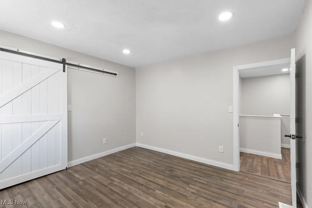 Unfurnished bedroom featuring dark wood-style flooring, recessed lighting, and a barn door
