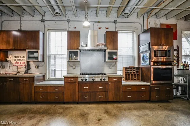 Kitchen featuring light countertops, appliances with stainless steel finishes, healthy amount of natural light, and wall chimney exhaust hood