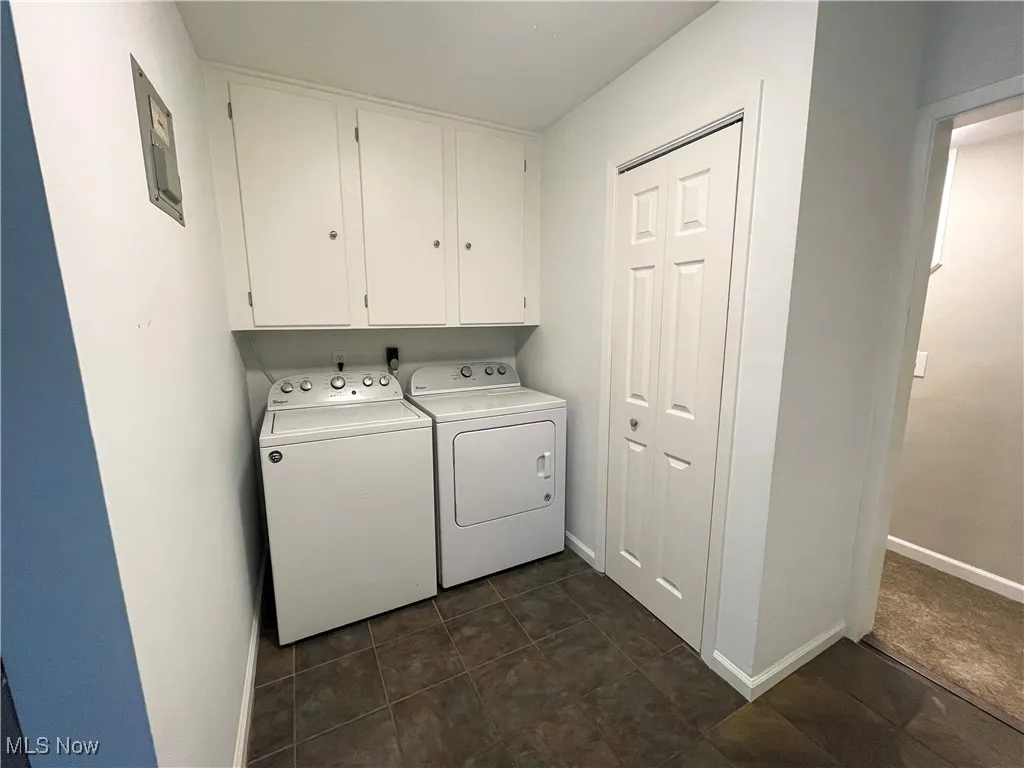 Washroom featuring washing machine and dryer, cabinet space, dark tile patterned floors, and electric panel