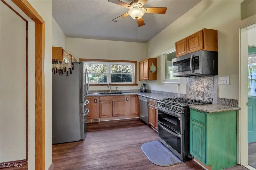Kitchen featuring appliances with stainless steel finishes, dark wood finished floors, ceiling fan, backsplash, and brown cabinetry