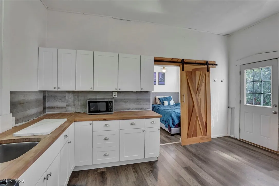Kitchen featuring white cabinetry, dark wood-style flooring, stainless steel microwave, and a barn door