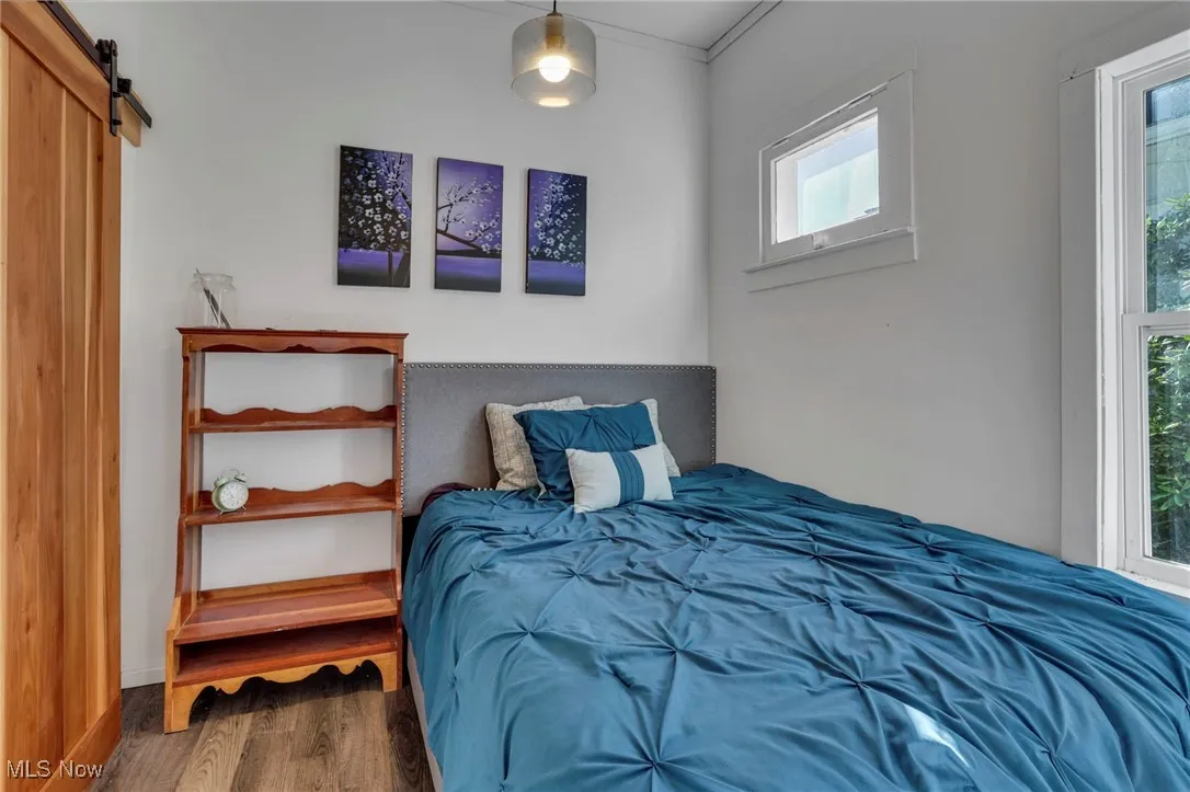 Bedroom with a barn door, wood finished floors, and ornamental molding