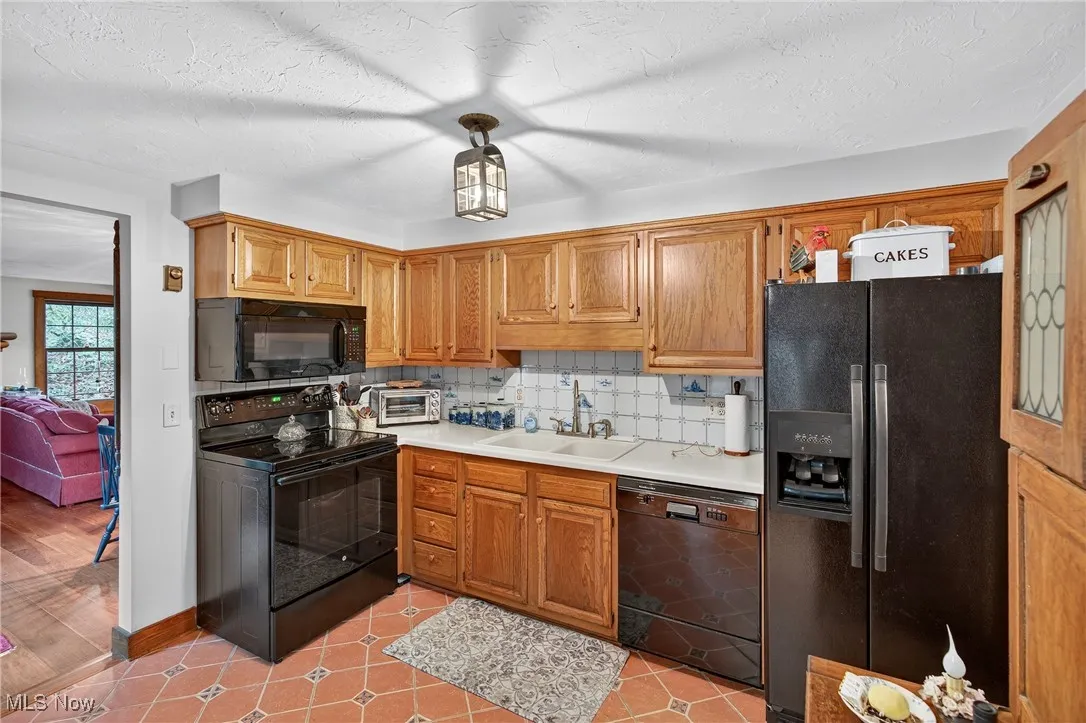Kitchen with tasteful backsplash, black appliances, light countertops, a textured ceiling, and light tile patterned floors