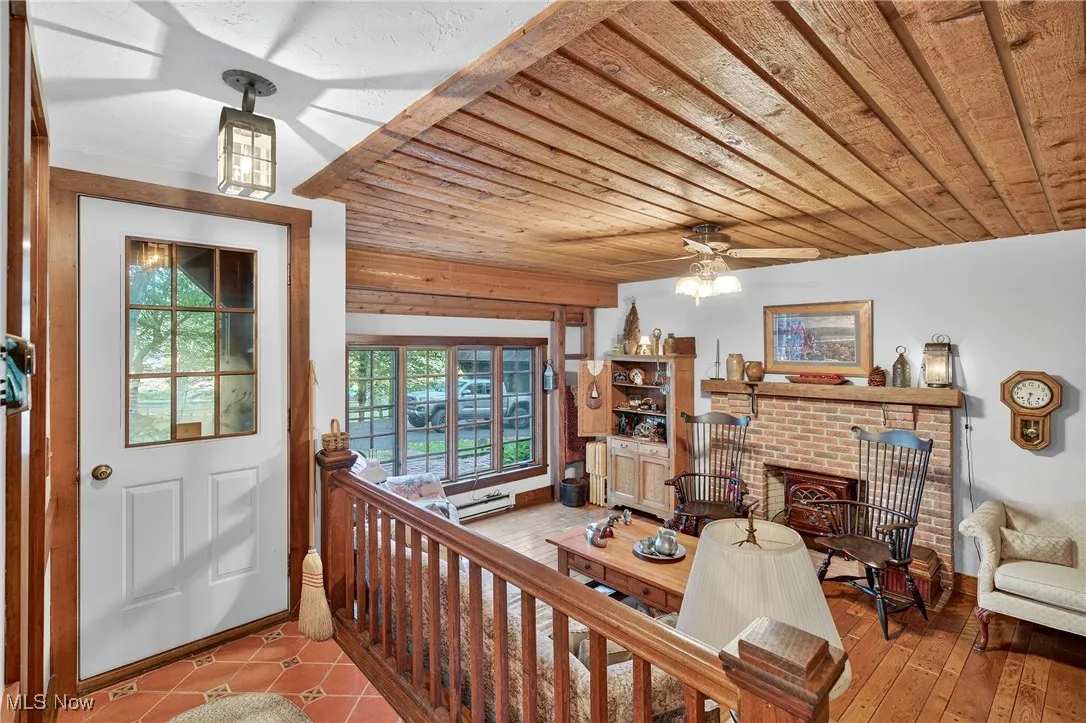 Entry onto den featuring wooden ceiling, a brick fireplace, a baseboard heating unit, and ceiling fan