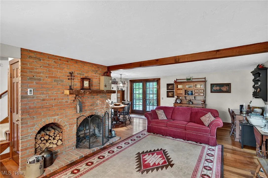 Living room with wood finished floors, a brick fireplace, beamed ceiling, and french doors