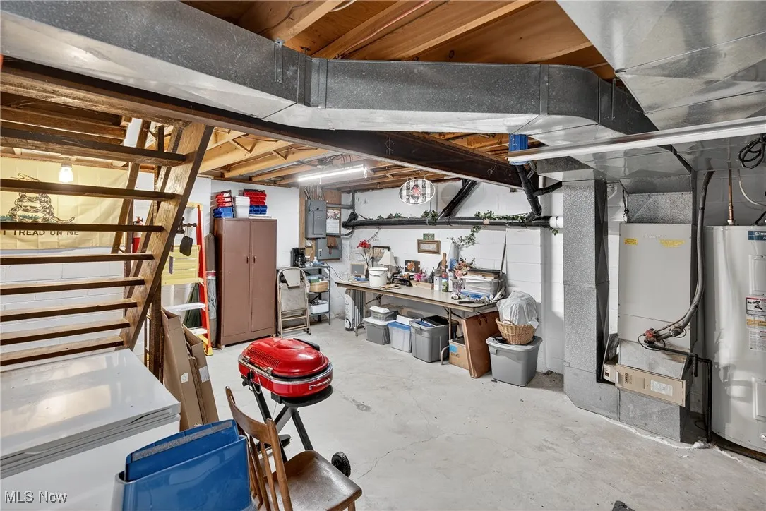 Unfinished basement with water heater, heating unit, white refrigerator, and electric panel