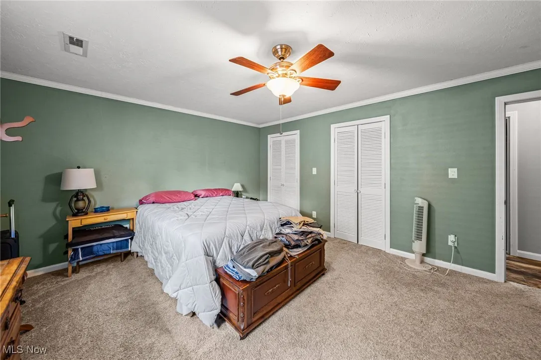 Carpeted bedroom featuring two closets, crown molding, a ceiling fan, and a textured ceiling