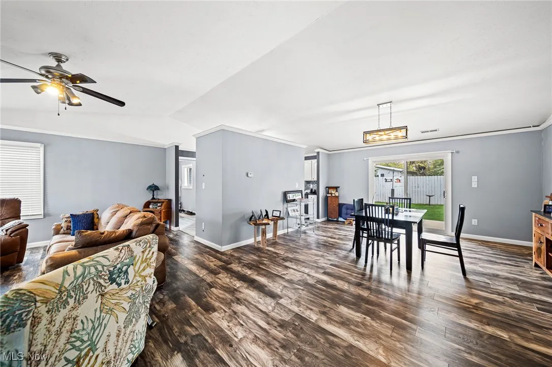 Dining space featuring dark wood-style floors, vaulted ceiling, ceiling fan, and crown molding