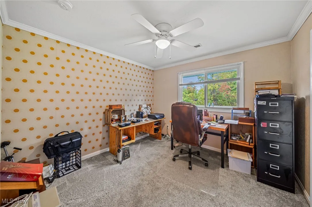 Office with wallpapered walls, ornamental molding, light carpet, and ceiling fan