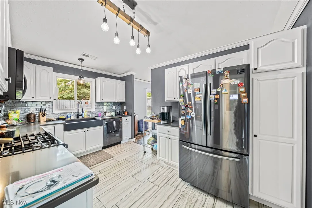 Kitchen with backsplash, freestanding refrigerator, hanging light fixtures, white cabinetry, and healthy amount of natural light