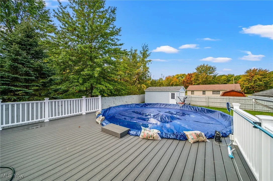 Wooden terrace featuring an outdoor structure, a fenced backyard, and view of scattered trees