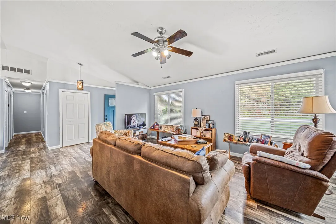 Living room featuring wood finished floors, ceiling fan, lofted ceiling, and crown molding