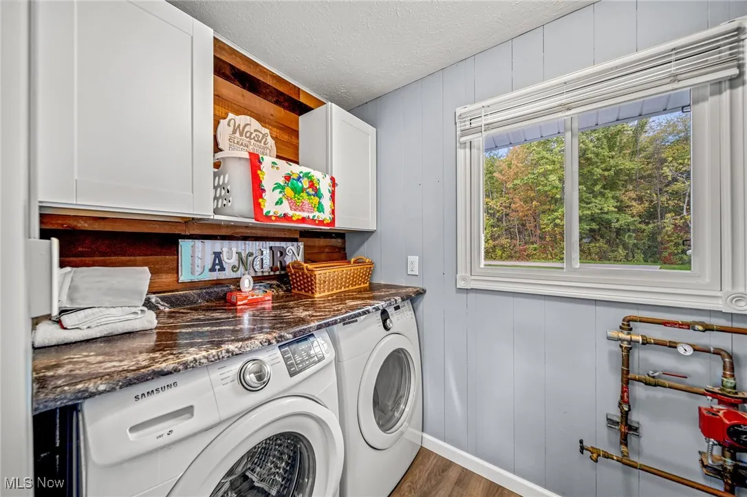 Washroom featuring wooden walls, cabinet space, washer and clothes dryer, dark wood-style floors, and a textured ceiling