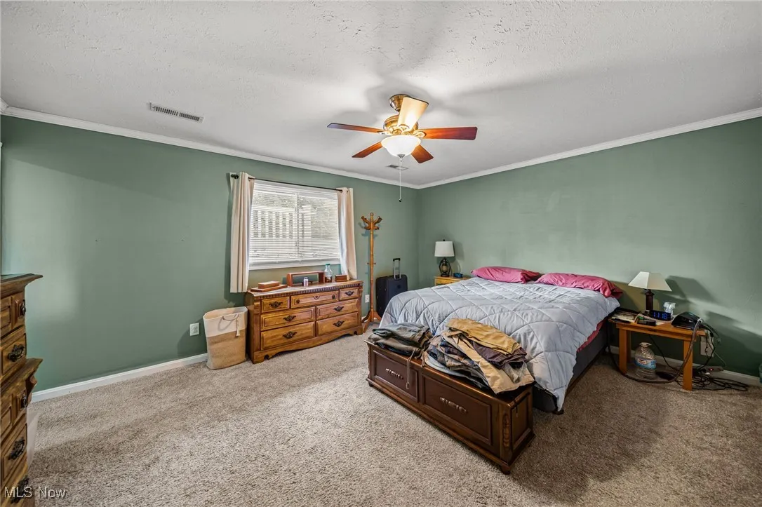 Carpeted bedroom featuring a textured ceiling, ceiling fan, and ornamental molding