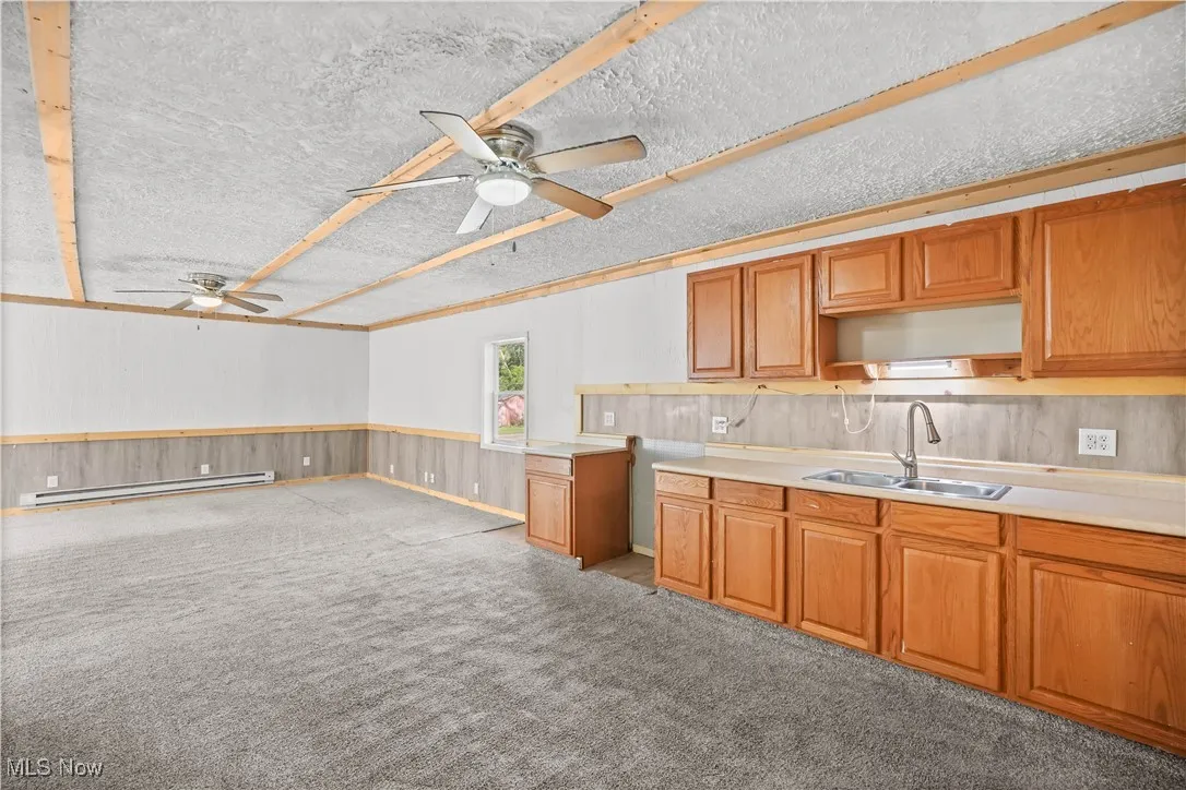 Kitchen with ceiling fan, open floor plan, a wainscoted wall, wood walls, and light countertops