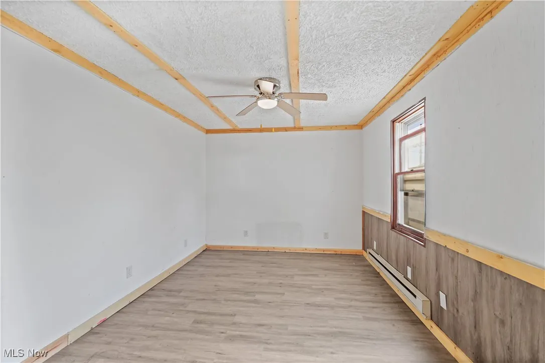 Spare room with a baseboard radiator, light wood finished floors, ceiling fan, a textured ceiling, and crown molding