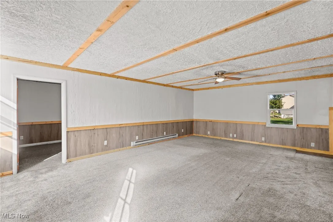 Unfurnished room with carpet flooring, wood walls, a baseboard radiator, ceiling fan, and a textured ceiling