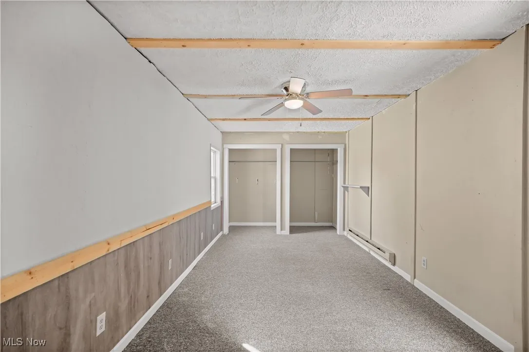 Unfurnished bedroom featuring multiple closets, light carpet, baseboard heating, a textured ceiling, and a ceiling fan