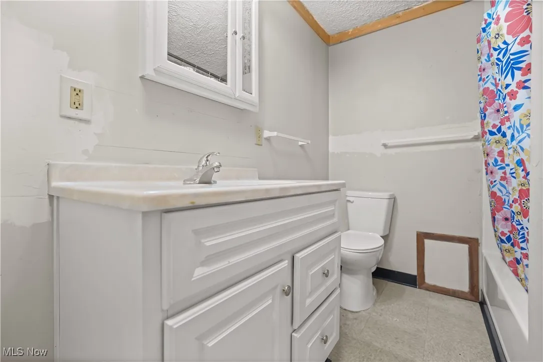 Full bathroom with vanity, shower / bath combo, and a textured ceiling