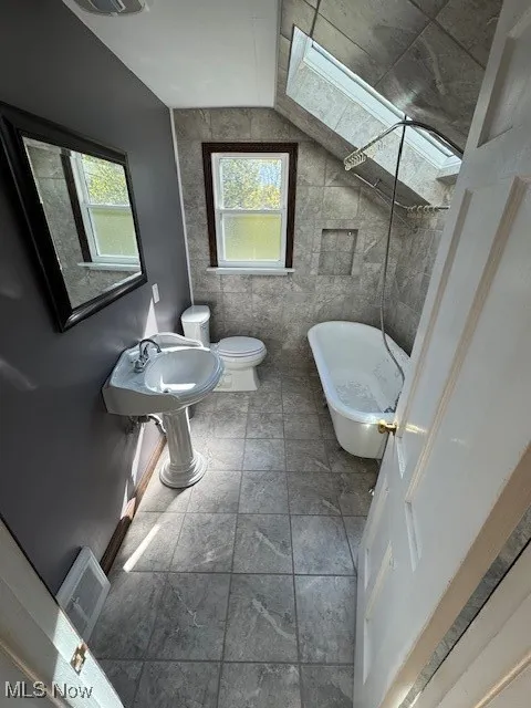 Full bath with a skylight, a freestanding bath, and tile walls