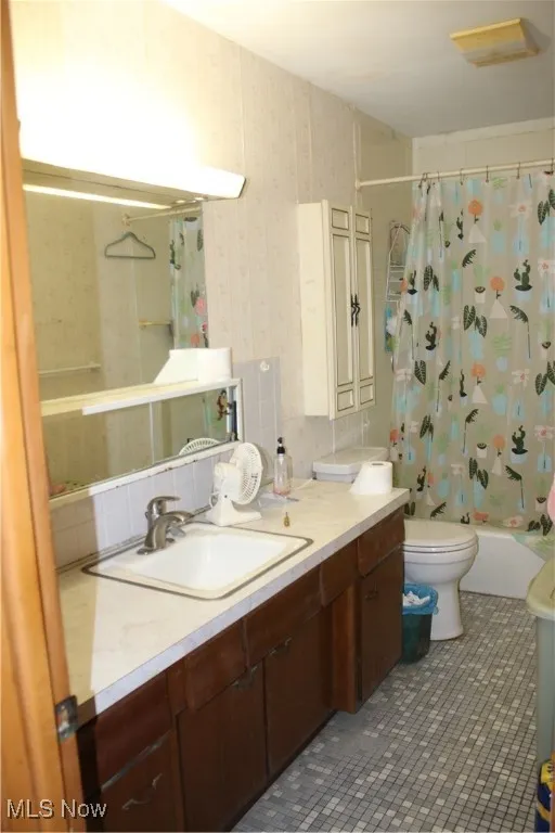 Full bathroom with shower / tub combo, vanity, decorative backsplash, dark tile patterned flooring, and wallpapered walls